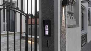 A security keypad and a wall-mounted light on a textured wall near a metal gate. - CA ’DEL RE’ SCARTOZZ Riva dei Bruti (Gavirate)
