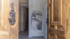 A hallway with a wooden door on the right and a wall with a black and white drawing of a street scene. - CA ’DEL RE’ SCARTOZZ Riva dei Bruti (Gavirate)
