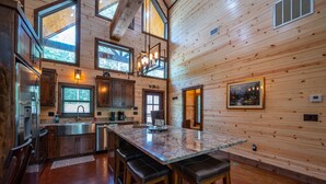 A spacious kitchen with wooden walls, a large island with bar stools, and a view of the outdoors through the windows. - # Kick Back Shack  ## Luxury Broken Bow Cabin with Hot Tub, Pool Table, EV Charg (Broken Bow)