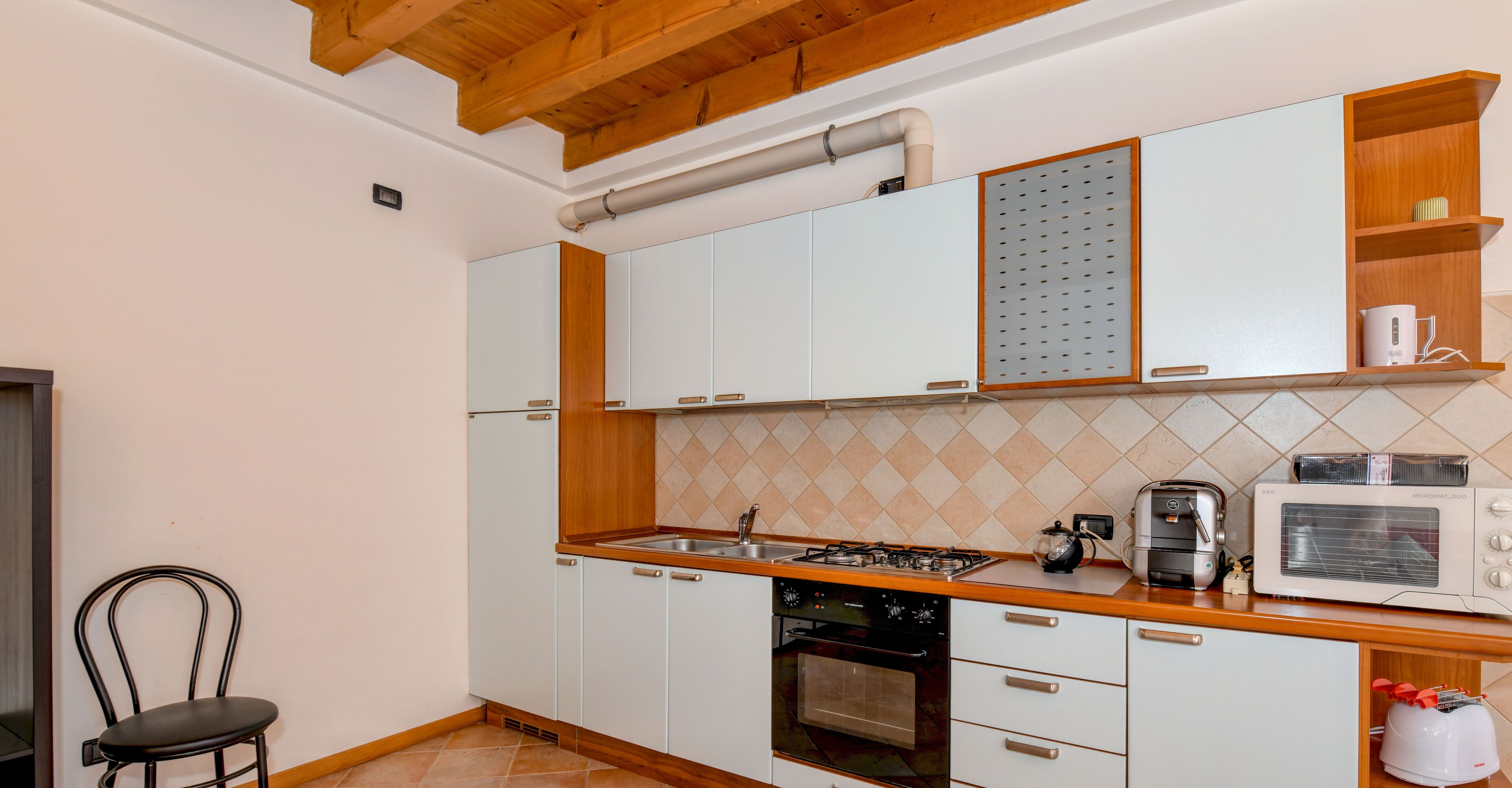 Une cuisine avec des meubles blancs, un plan de travail en bois, une cuisinière, un four, un four à micro-ondes et un évier.
