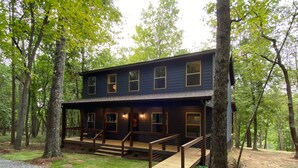 Une cabane à deux étages avec une terrasse en bois, entourée d’arbres.