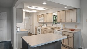 Een moderne keuken met lichte houten keukenkastjes, een centraal eiland, een magnetron en een vaatwasser.