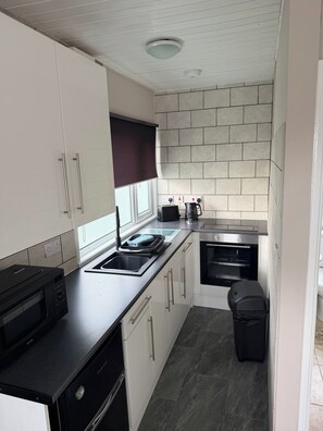 A compact kitchen with white cabinets, a black countertop, a built-in oven, and a trash bin. - Chalet 91A South Shore Bridlington, Sleeps 4 (Bridlington)