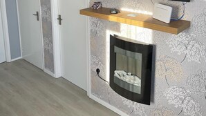 A modern living room with a flat-screen TV mounted on the wall, a fireplace below, and a wooden shelf with a remote control. - Chalet 91A South Shore Bridlington (Bridlington)