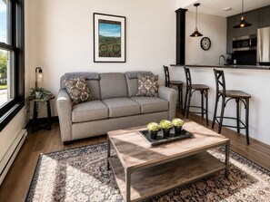 Een woonkamer met een bank, een salontafel en een keukenbar met barstoelen.