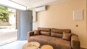 A modern living room with a brown leather sofa, two wooden side tables, and a glass door leading outside. - Urban Loft - Stylish One Bedroom Apartment (Κέρκυρα)