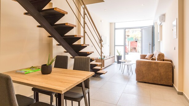 A modern interior with a wooden dining table, a sofa, a staircase, and a view to the outside. - Urban Loft - Stylish One Bedroom Apartment (Κέρκυρα)