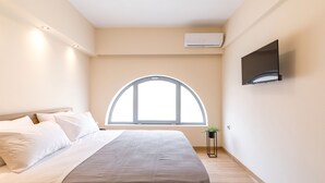 A bedroom with a bed, a large window, an air conditioning unit, and a mounted TV. - Urban Loft - Stylish One Bedroom Apartment (Κέρκυρα)