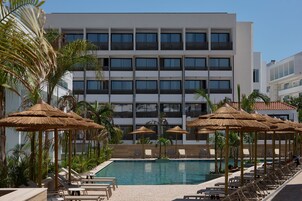 Un hotel moderno con piscina, tumbonas y sombrillas de paja.
