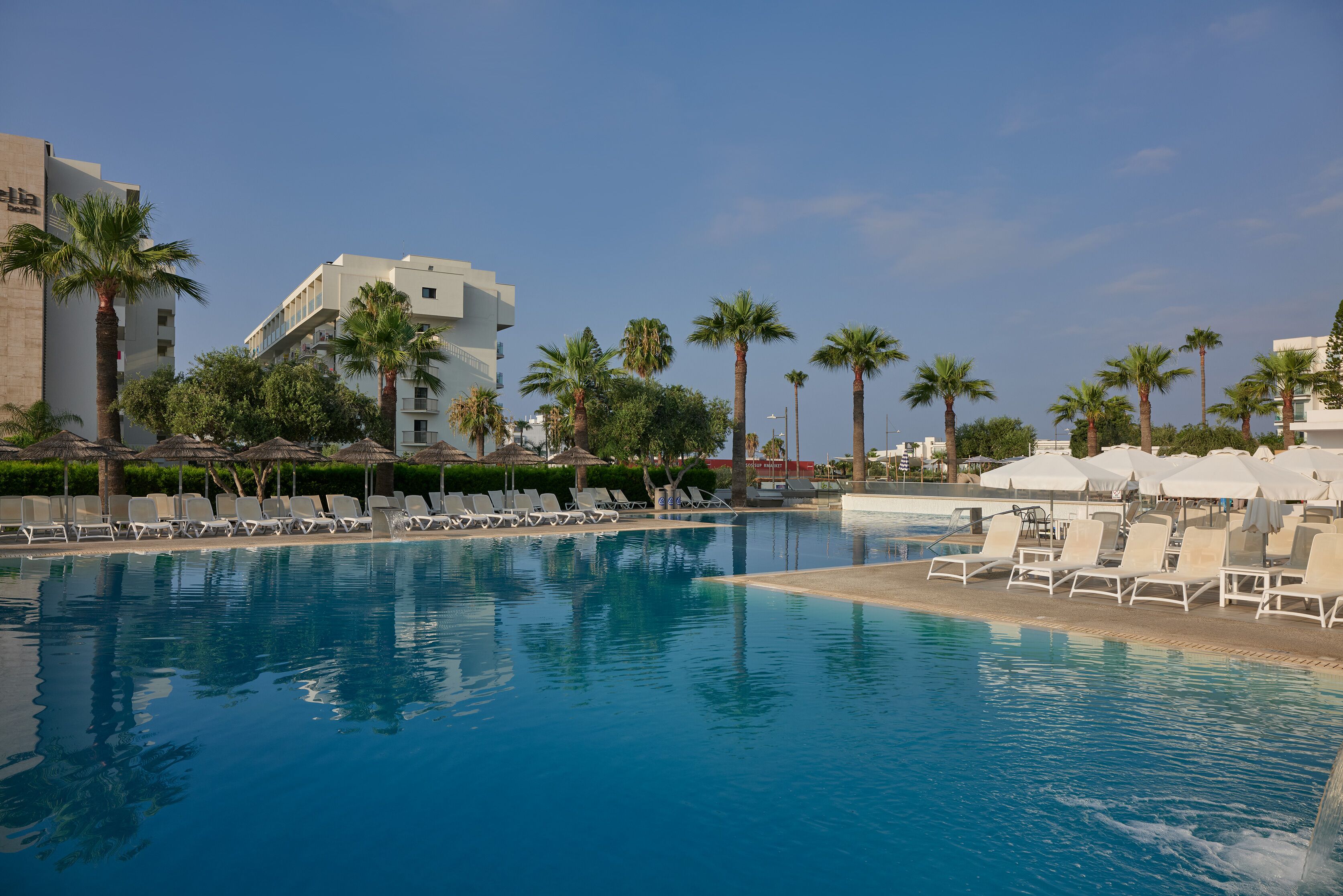 Ein Swimmingpool mit Liegestühlen und Palmen, umgeben von Gebäuden.