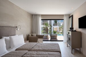 A hotel room with a large bed, a TV, a desk, and a view of the pool and buildings outside.