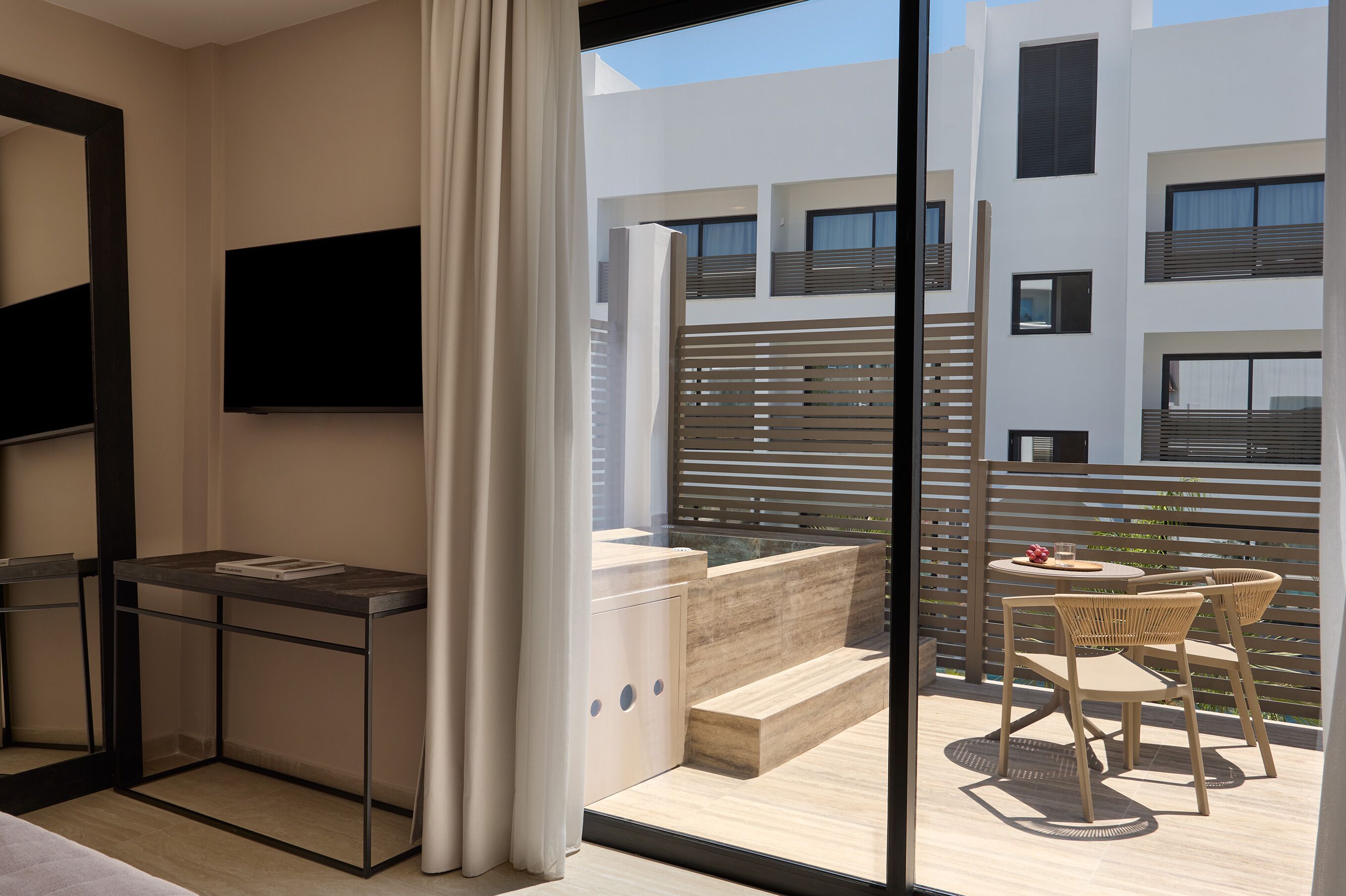 Un appartement moderne doté d’un balcon, d’un téléviseur à écran plat et d’un coin repas avec des meubles en osier.