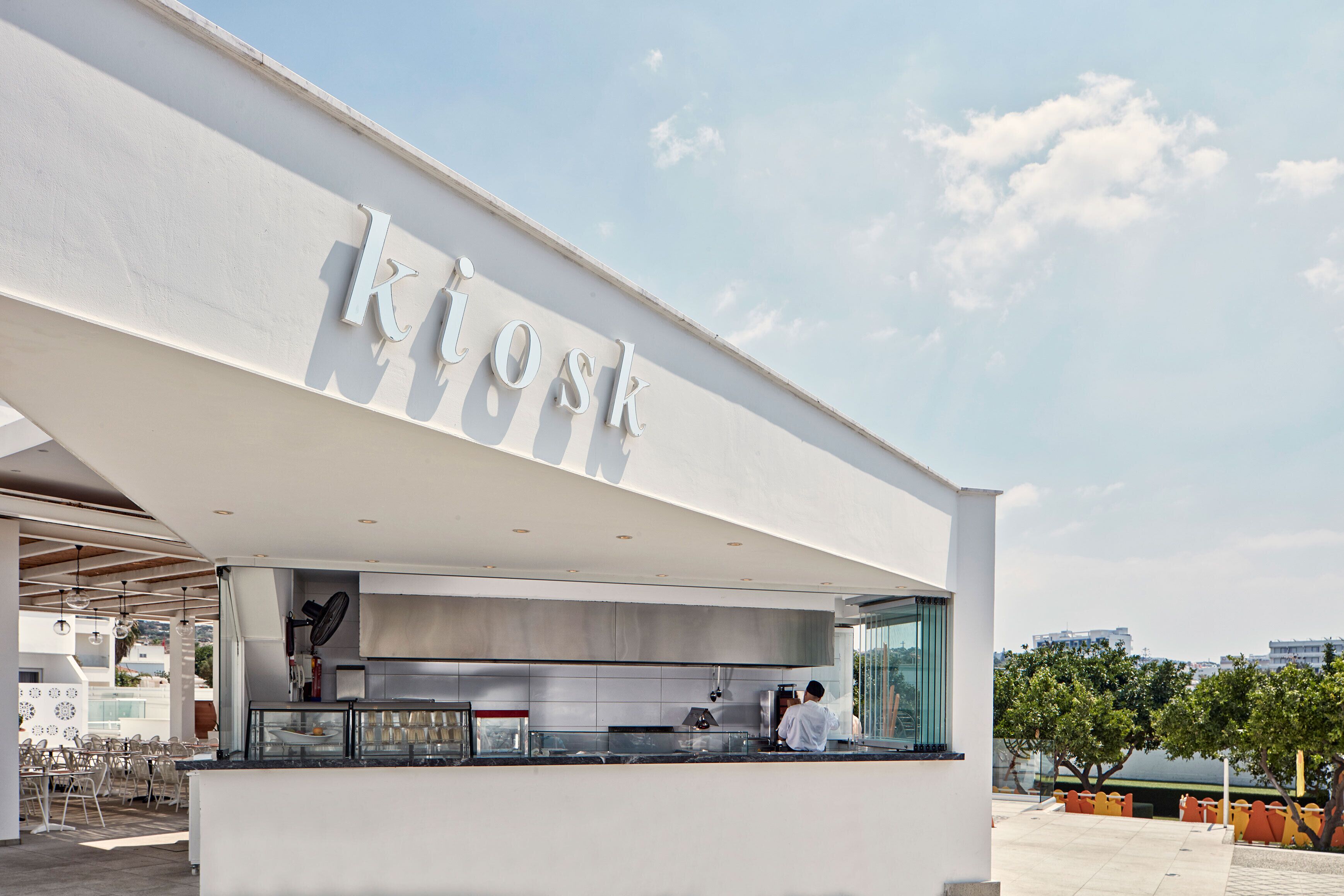 Een modern buitencafe met een helder uitzicht op de lucht en een bord waarop 'Kiosk' staat.