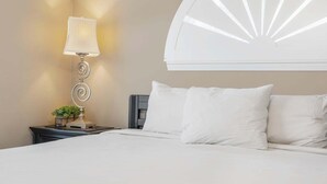 Un lit bien fait, avec du linge de lit blanc, une lampe fixée au mur et un élément décoratif mural.