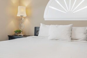 Un lit bien fait, avec du linge de lit blanc, une lampe fixée au mur et un élément décoratif mural.