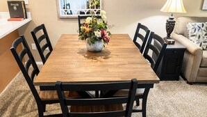Une table à manger avec des chaises, un vase de fleurs, une lampe et un canapé dans une pièce recouverte d’un tapis.