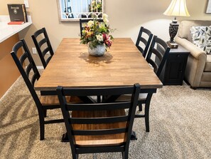 A dining table with chairs, a vase with flowers, a lamp, and a sofa in a room with carpet.