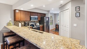 Una cocina con encimeras de granito, gabinetes de madera, electrodomésticos de acero inoxidable y una barra con taburetes.