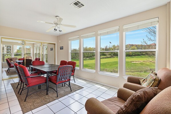 A spacious room with a dining table and chairs, large windows with a view of a golf course, a ceiling fan, and a cozy seating area with a couch. - 2 Bedroom, 2 Bath Walk-in Golf Condo featuring Whirlpool Tub & Sunroom with Course View (Branson)