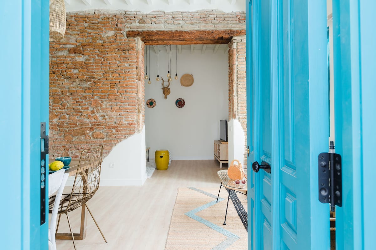 Una habitación con pared de ladrillo, puerta azul, techo blanco y suelo de madera.