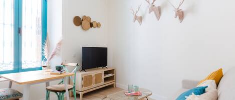 A living room with a TV, a sofa, a coffee table, and a dining area with chairs and a table.