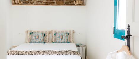 Un dormitorio con pared de ladrillo, cama con ropa de cama estampada, mesita de noche pequeña y ventana con marco azul.