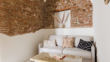 A living room with a brick wall, a sofa with patterned cushions, and a glass coffee table with books.