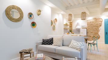 Una sala moderna con un sofá de color gris claro, una mesa de centro redonda y una silla de mimbre. Objetos decorativos tejidos se exhiben en las paredes.