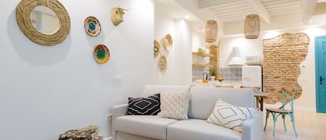 A modern living room with a light grey sofa, a round coffee table, and a wicker chair. Decorative woven items are displayed on the walls.