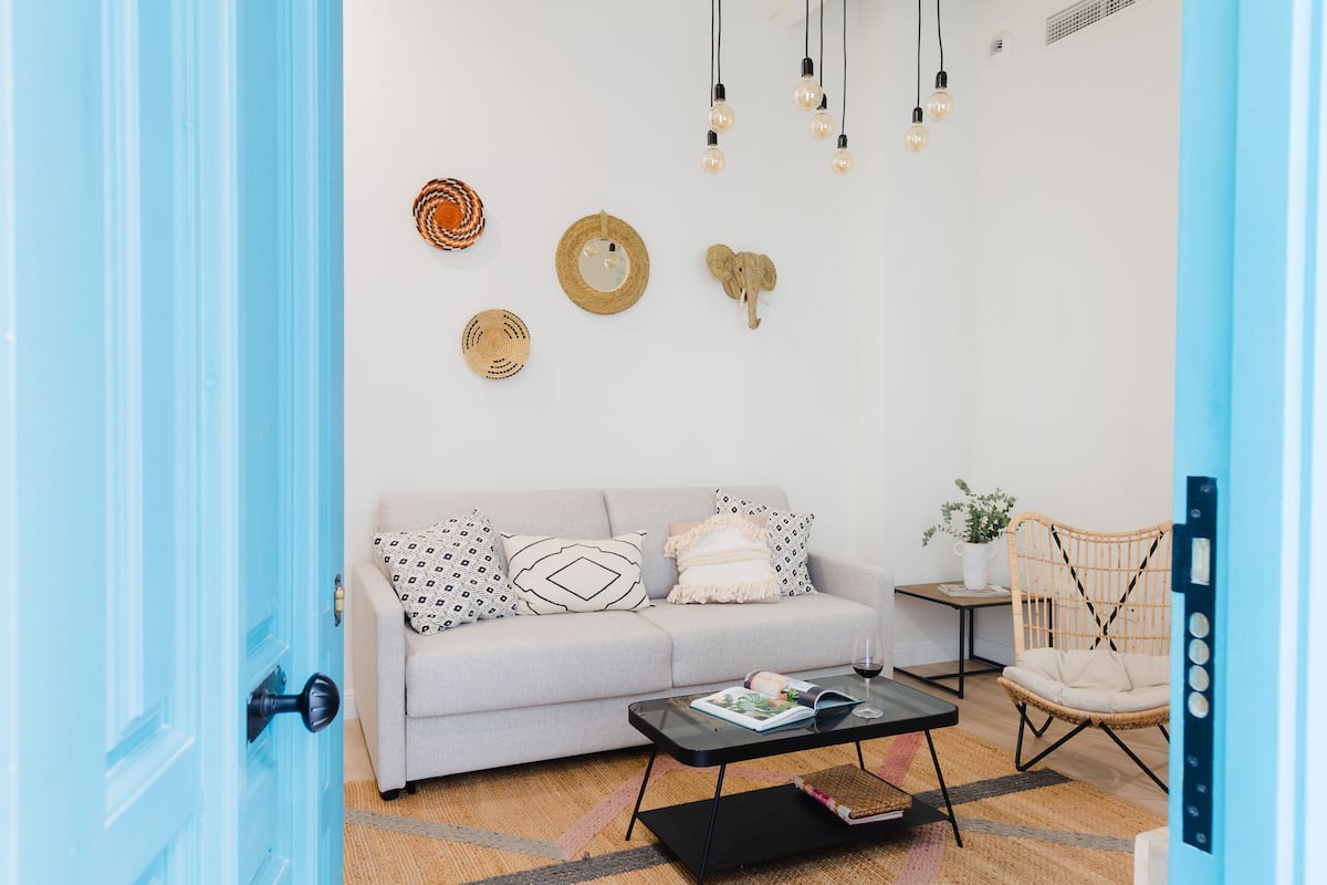 Sala de estar con un sofá gris claro, una mesa de centro negra y una silla de mimbre. Decoración en las paredes, incluyendo una cesta tejida y un elefante de madera.