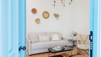 A living room with a light grey sofa, a black coffee table, and a wicker chair. There are wall decorations including a woven basket and a wooden elephant.