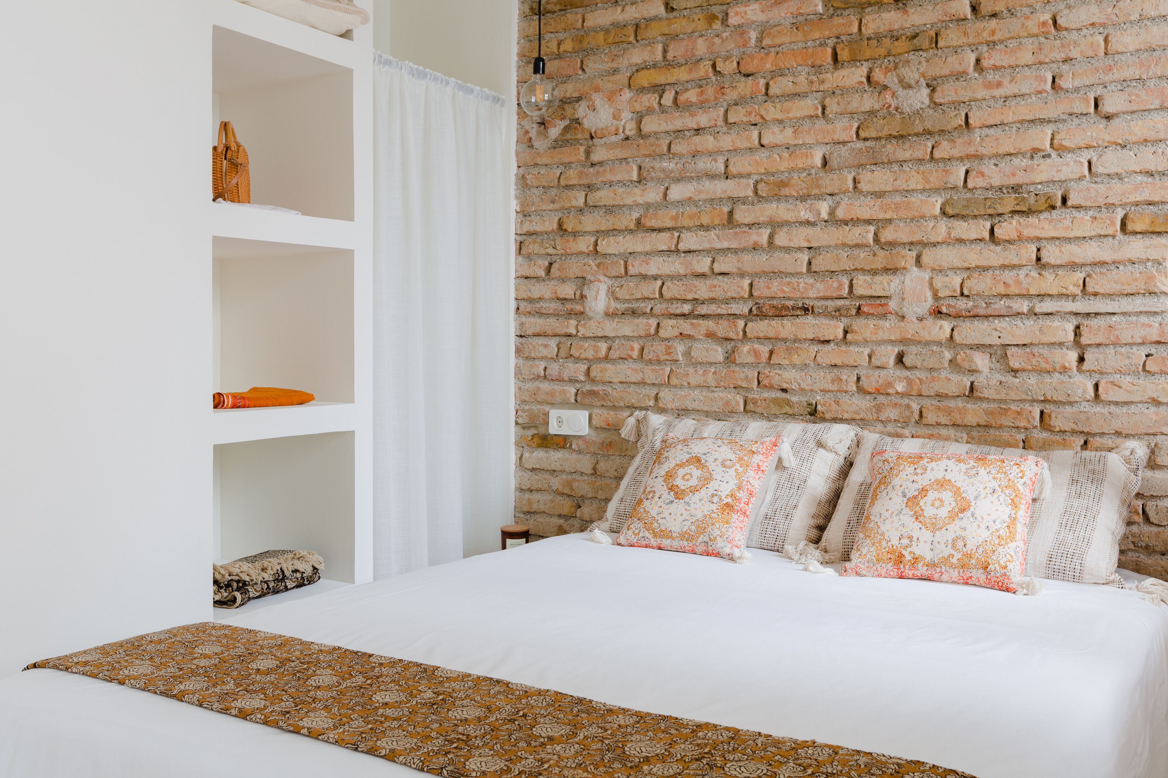 Un dormitorio con pared de ladrillo, cama con ropa de cama blanca y una manta decorativa.