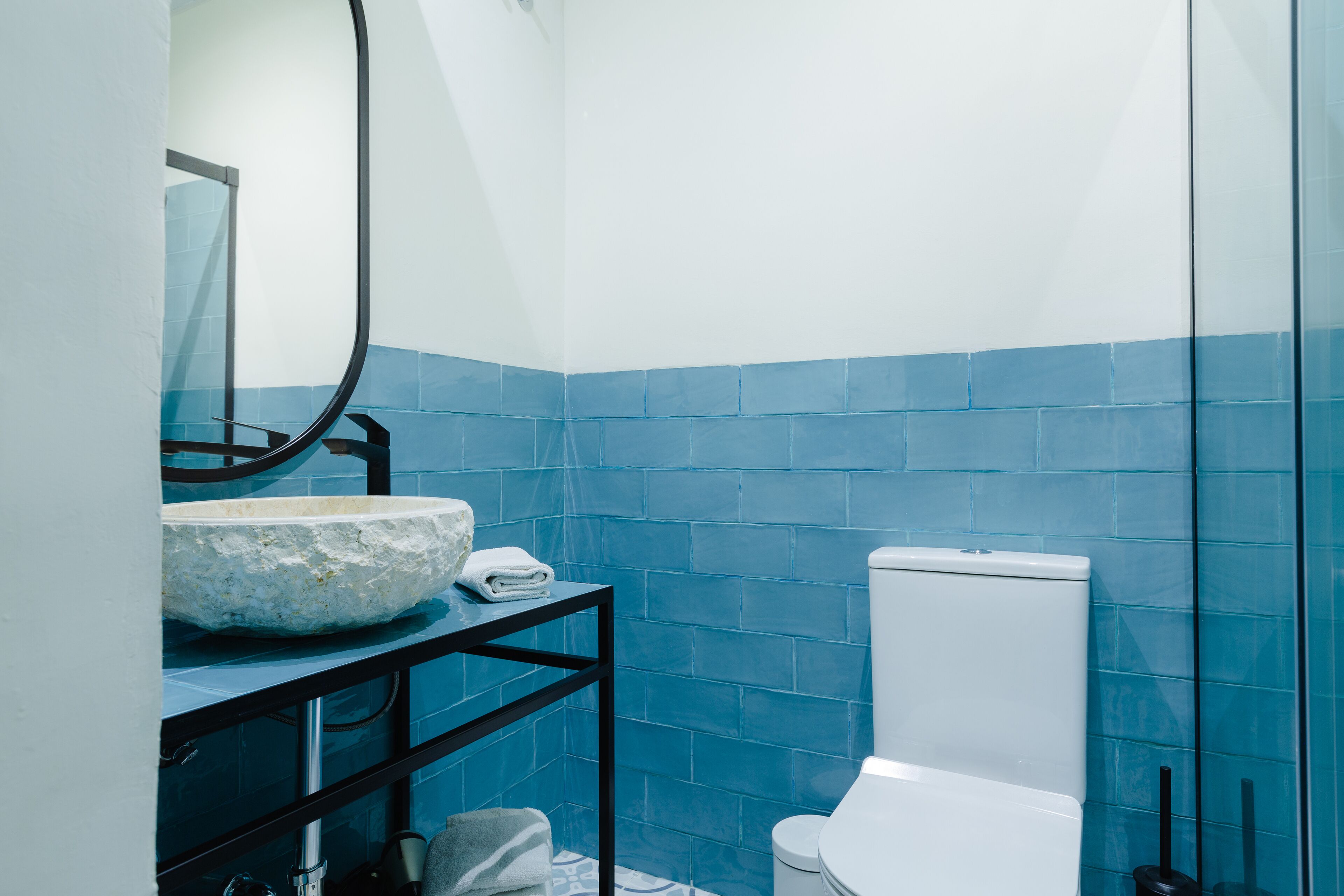 A bathroom with a white sink, blue tiles, a black metal shelf, and a white toilet.