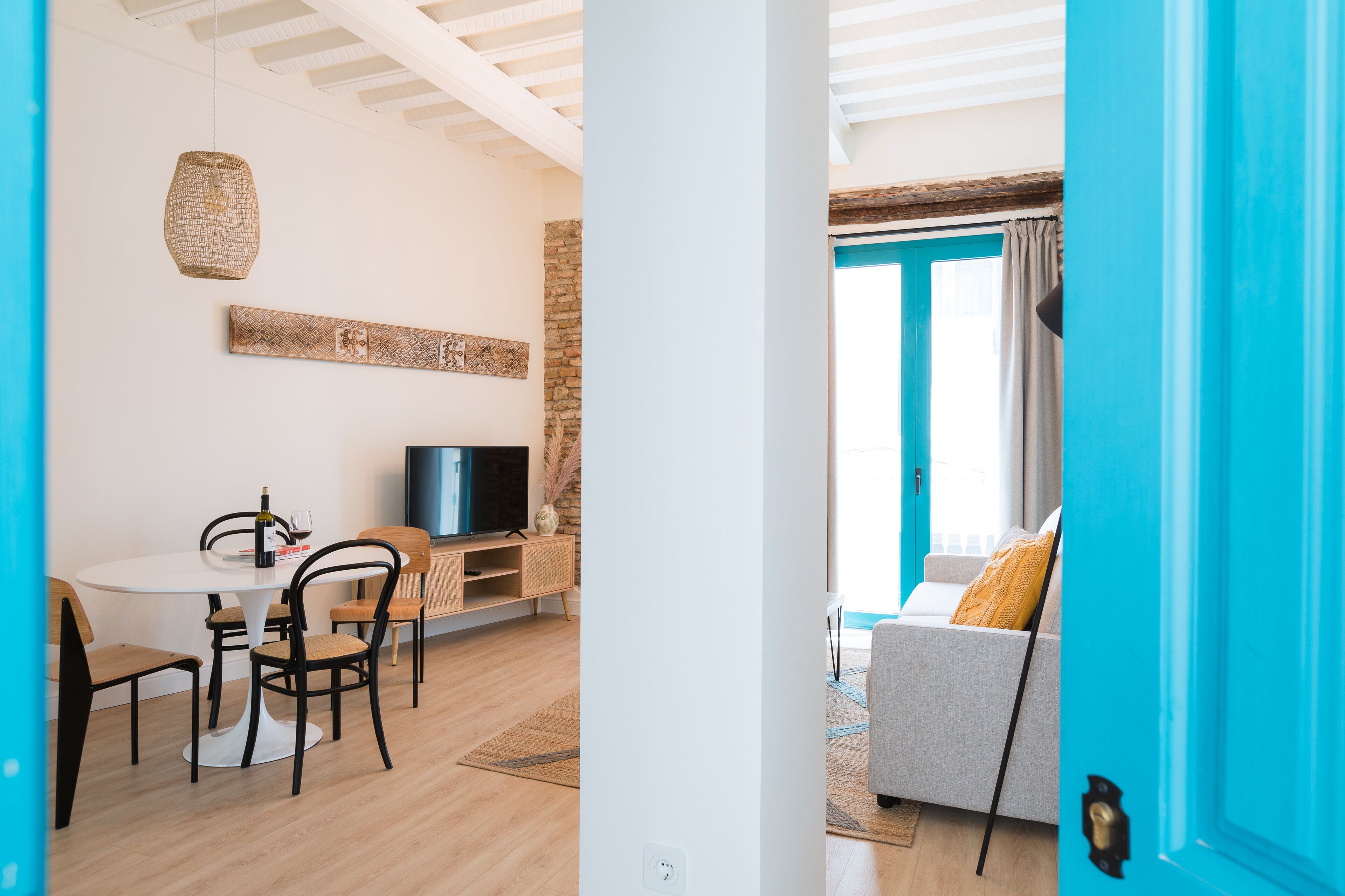 Uma sala de estar moderna com área de jantar, televisão e um sofá, com uma porta azul ao fundo.
