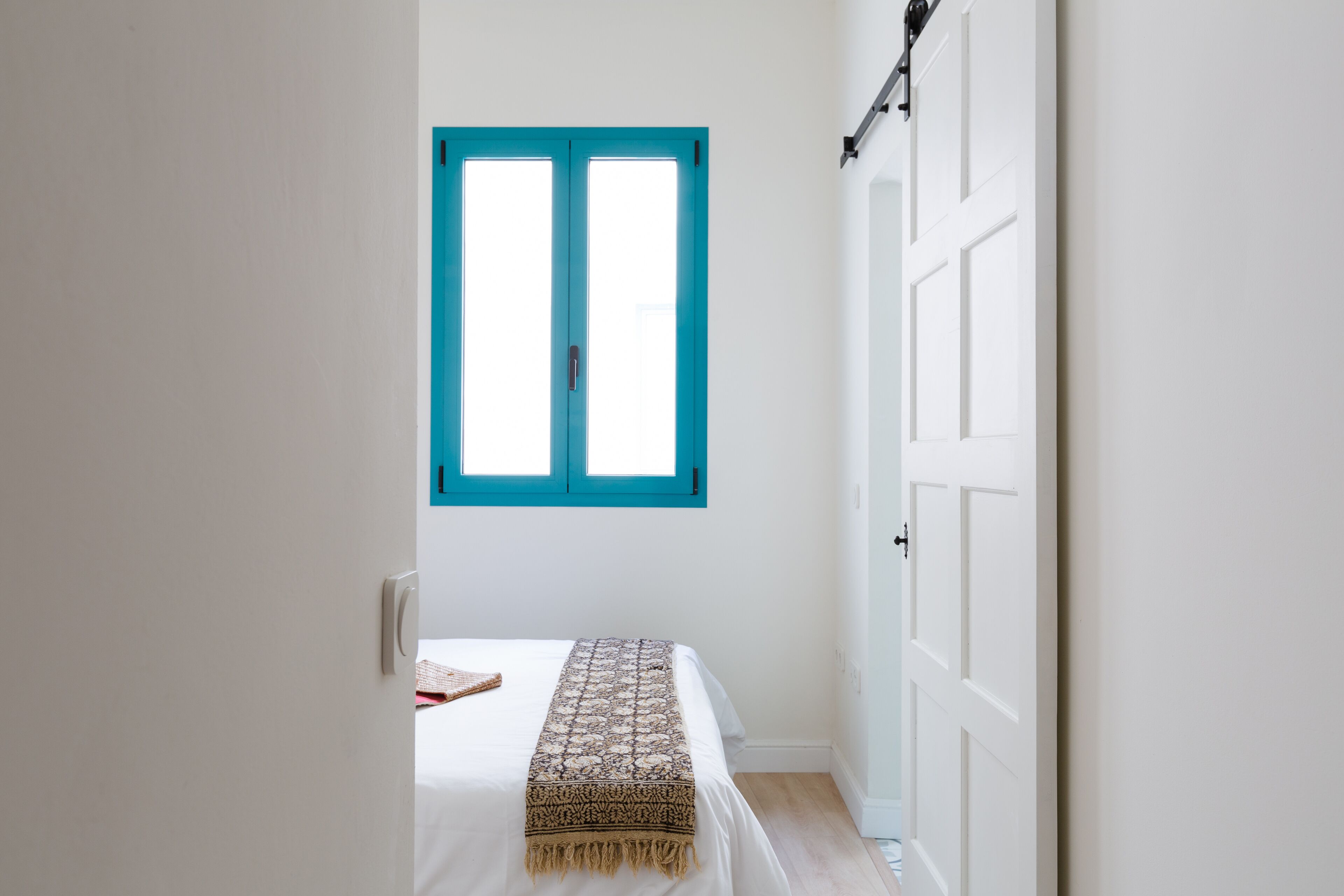 Een slaapkamer met een bed, een raam met blauwe luiken en een witte deur.