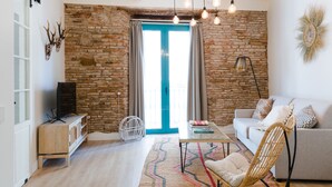 Un salon avec un mur en pierre, une porte bleue, un canapé, une table basse et un téléviseur posé sur un meuble en bois.