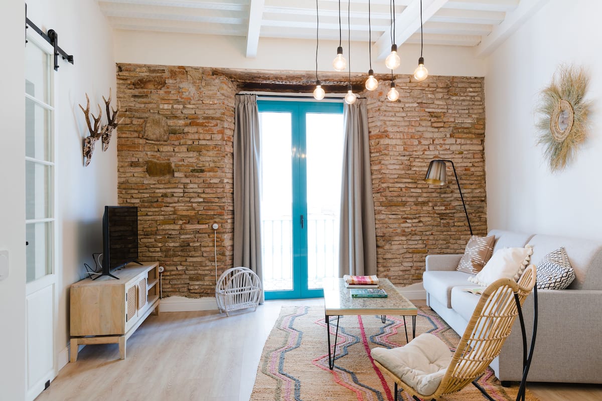 Una sala de estar con una pared de piedra, una puerta azul, un sofá, una mesita de centro y un televisor sobre un mueble de madera.