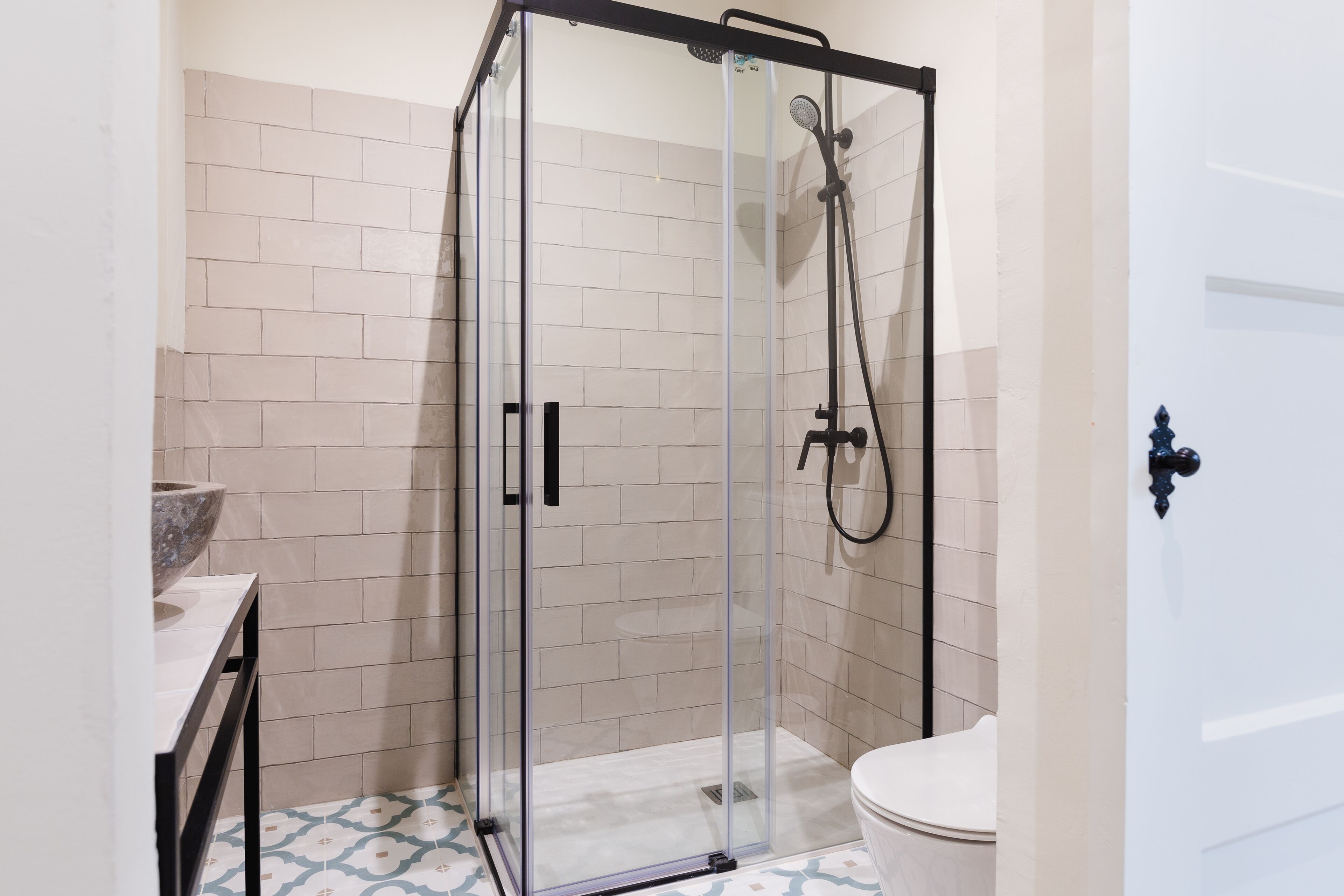 A glass-enclosed shower with a handheld showerhead, a white toilet, and a sink with a marble basin.