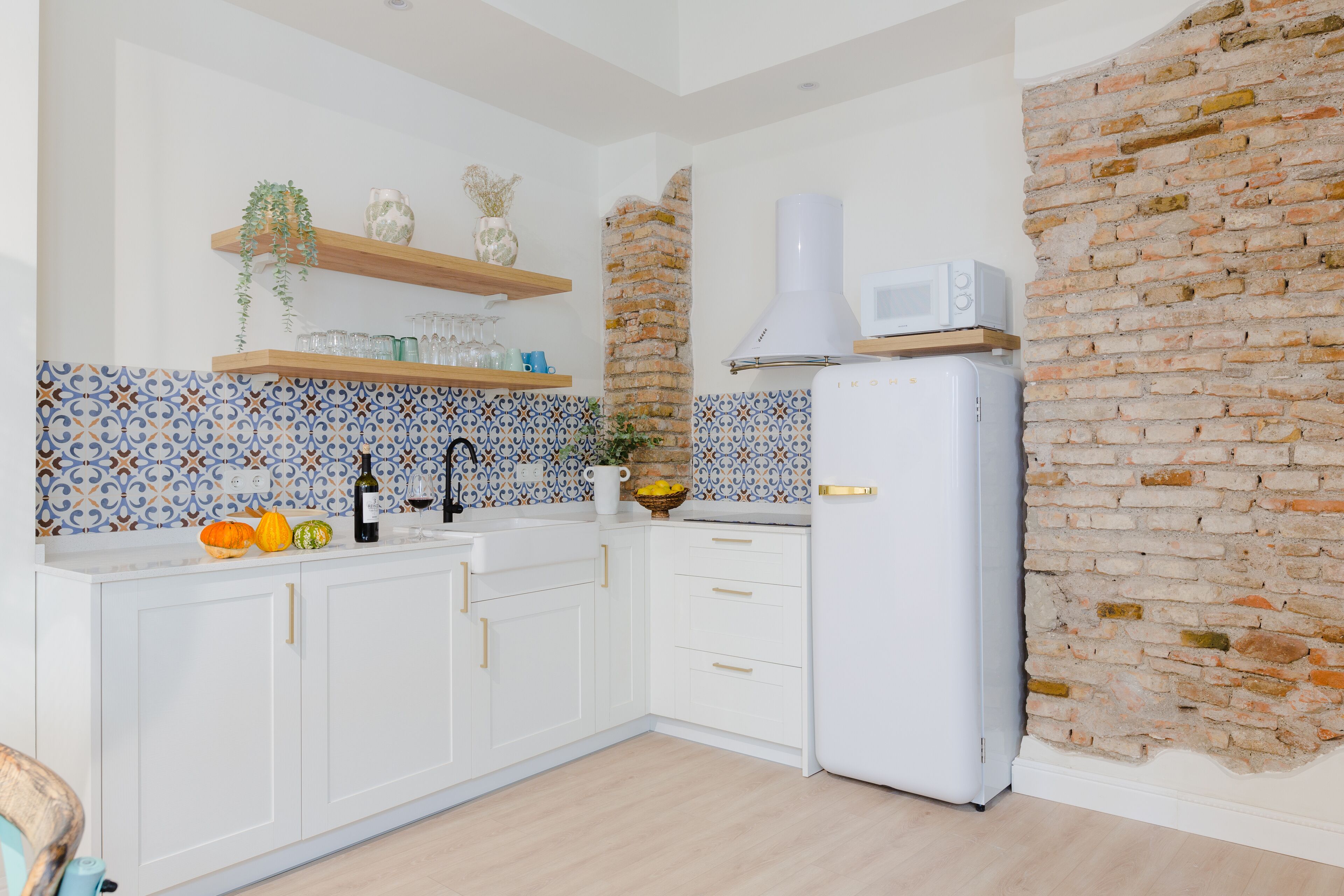 A modern kitchen with white cabinets, a brick wall, a microwave, and decorative items on the shelves.