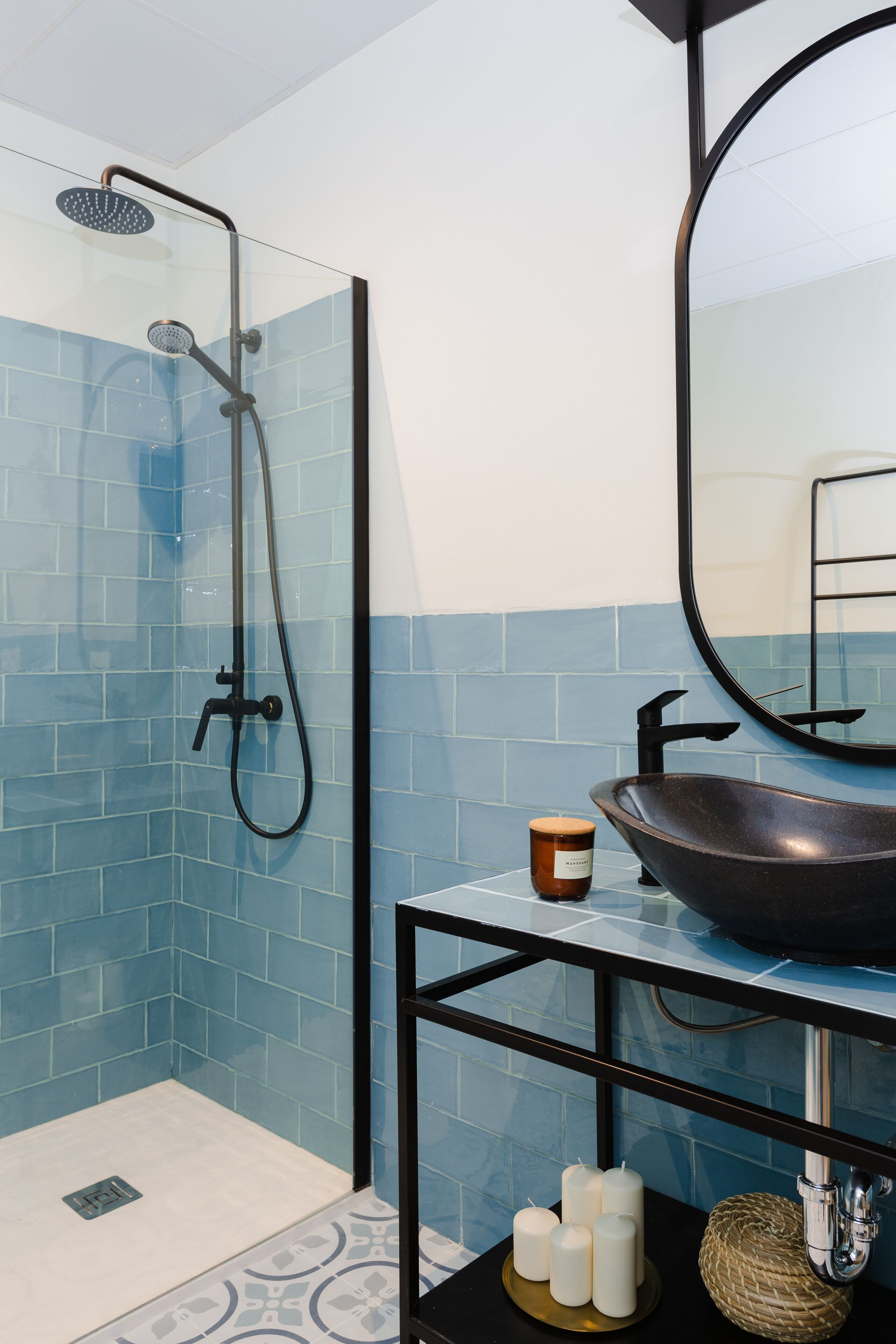 A bathroom with a glass shower enclosure, a black sink with a round basin, and a mirror above the sink.