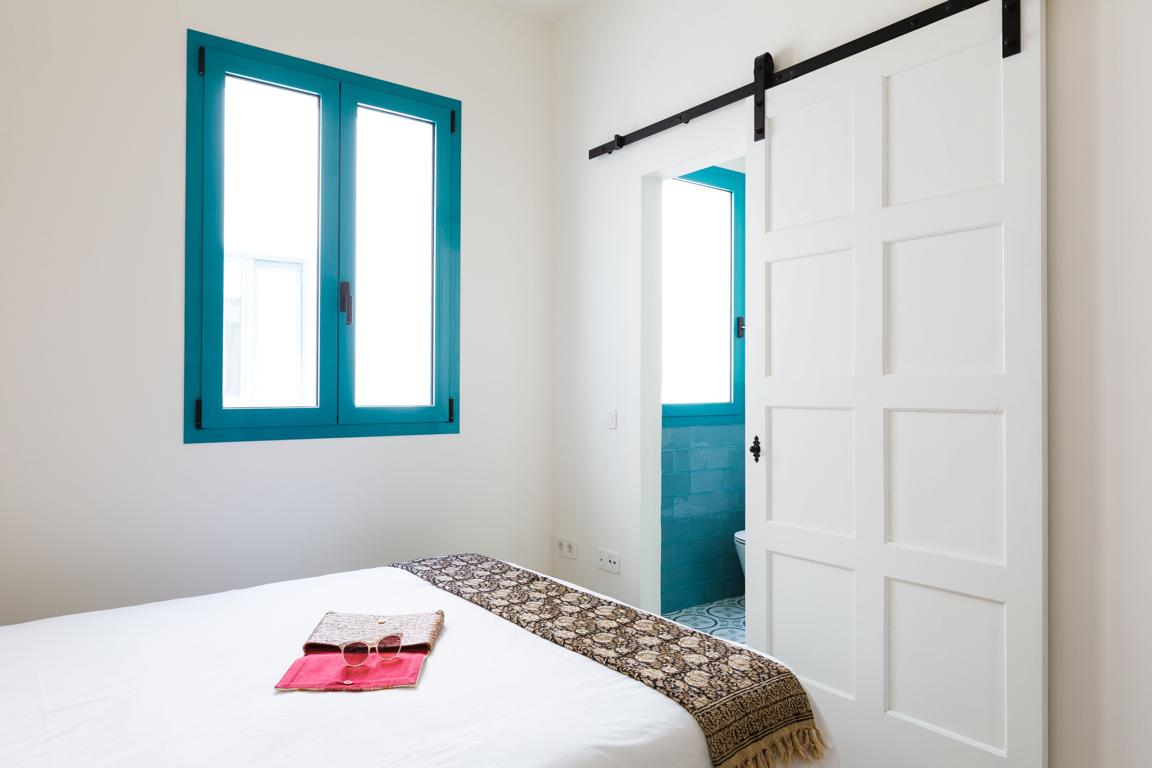 Une chambre à coucher avec un lit, une fenêtre, une porte et une salle de bain visible à travers une porte ouverte.