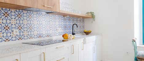 A kitchen with white cabinets, a patterned backsplash, and a wooden shelf above the sink.
