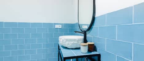 A bathroom with blue tiles, a white sink, a mirror, and a black shelf with a jar and a candle.