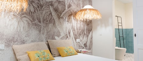 A bedroom with a bed, two pillows, a nightstand, a wall with a leaf pattern, and a door leading to a bathroom.