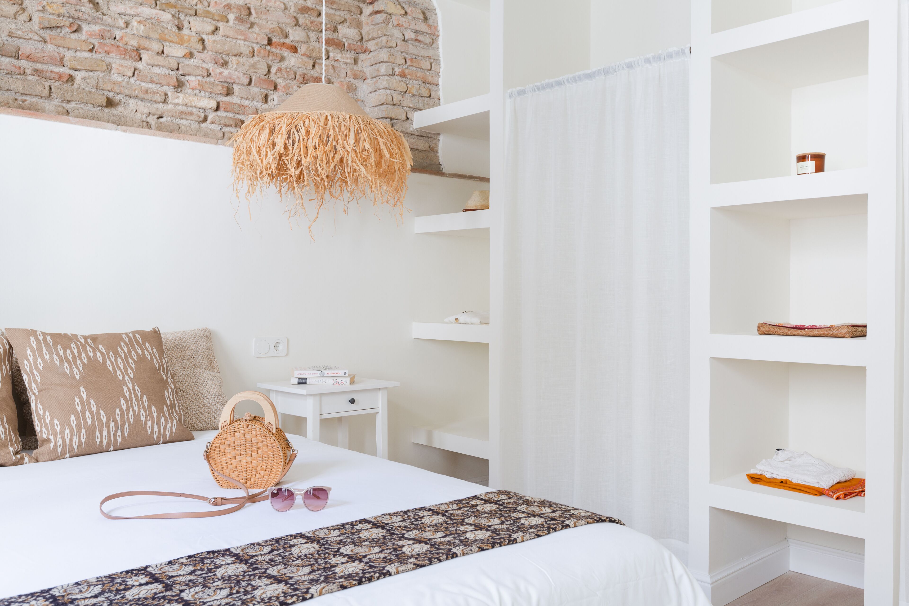 Ein Schlafzimmer mit Backsteinwand, einer Pendelleuchte, einem weißen Bett und einem weißen Kleiderschrank mit Regalen.