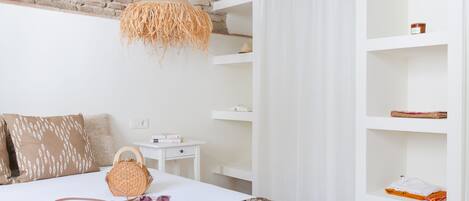 A bedroom with a brick wall, a hanging light fixture, a white bed, and a white wardrobe with shelves.
