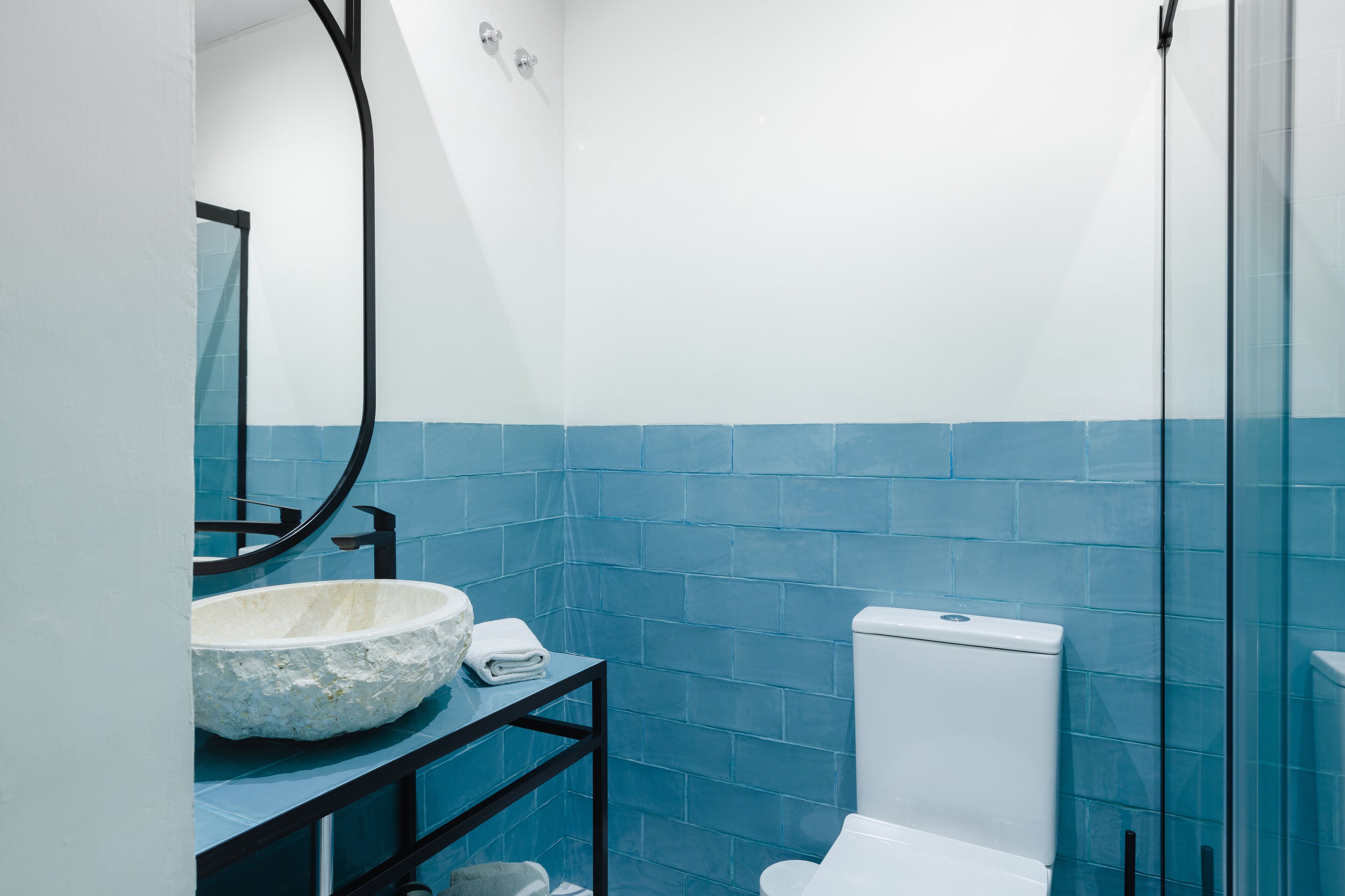 Un baño con inodoro blanco, lavamanos de piedra y paredes con azulejos azules.