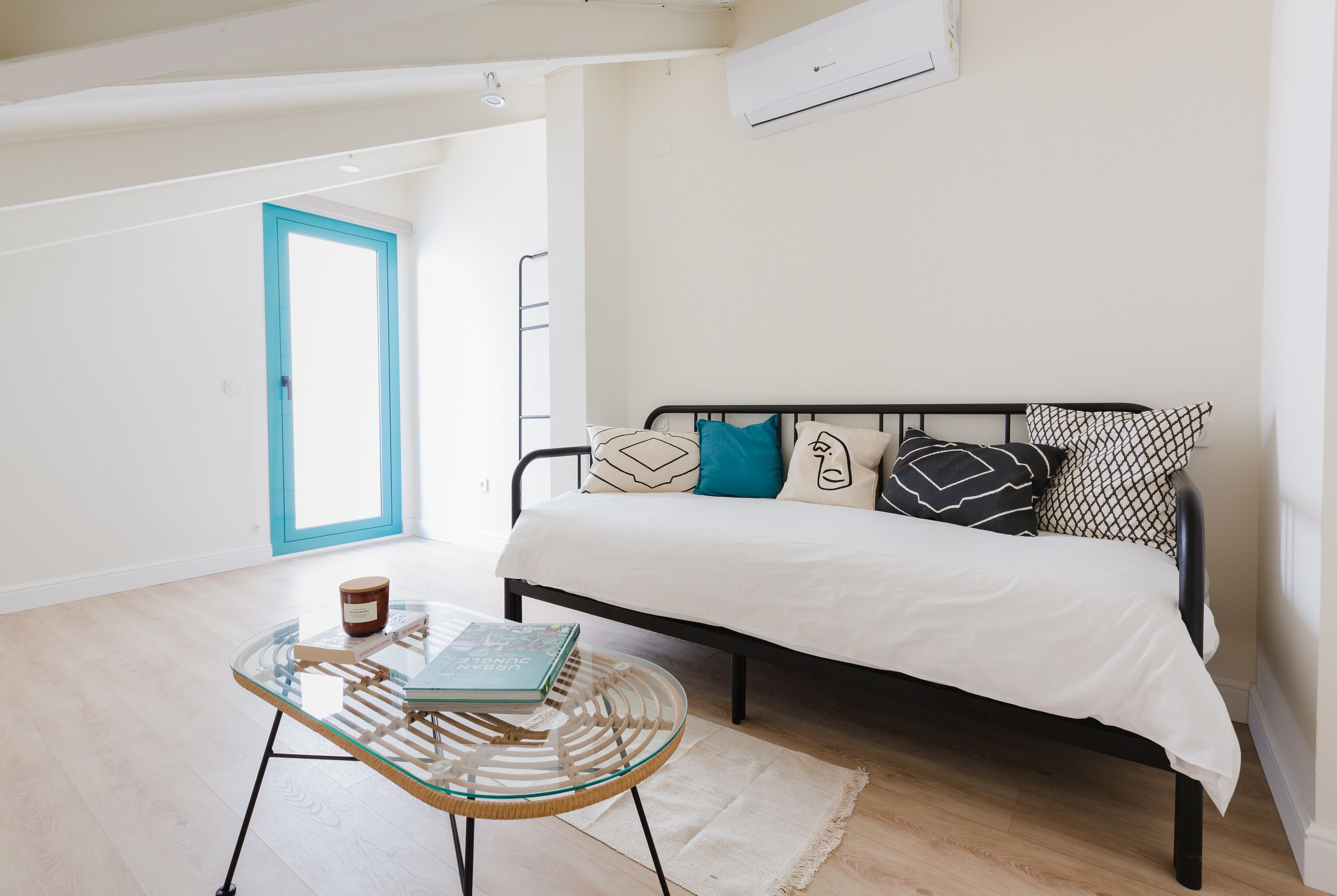A bedroom with a bed, a glass table with a book, and a white door.