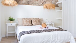 Une chambre avec un lit blanc, deux tables de chevet, un mur en briques et des lampes suspendues.