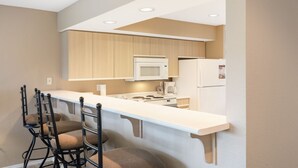 Una cocina moderna con encimera blanca, armarios de madera, microondas, estufa y refrigerador.